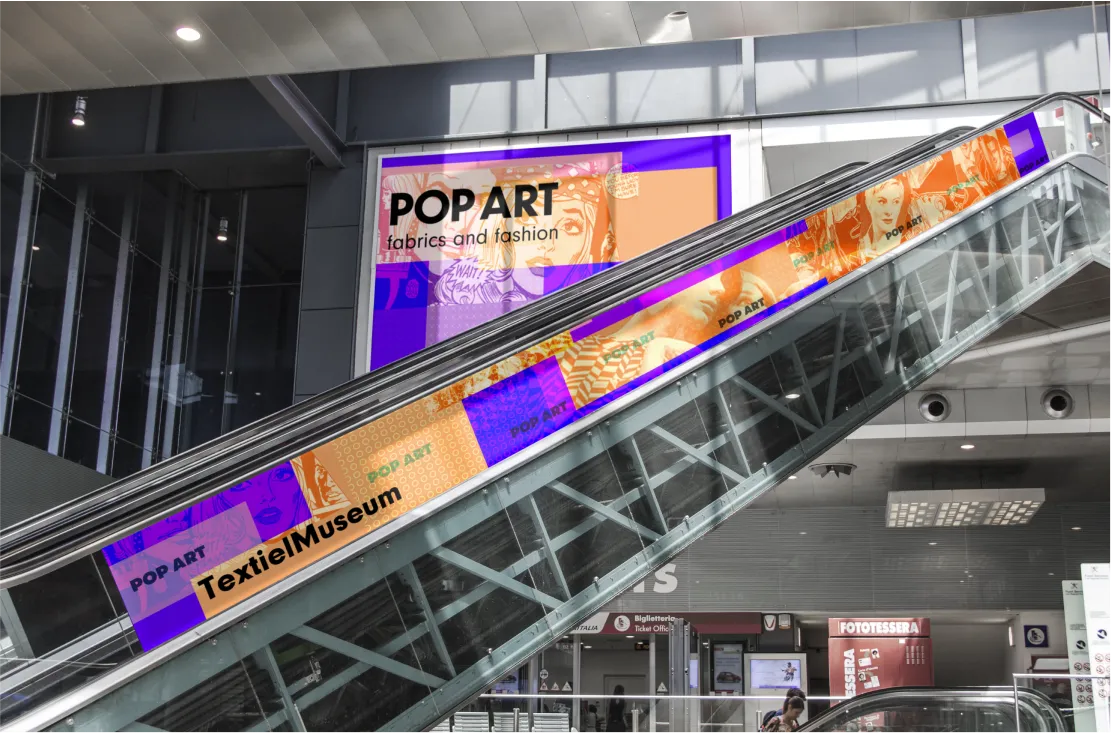Photo-realistic mockup of a mall escalator wrapped in 'Pop Art' branding, beneath a matching wall billboard.