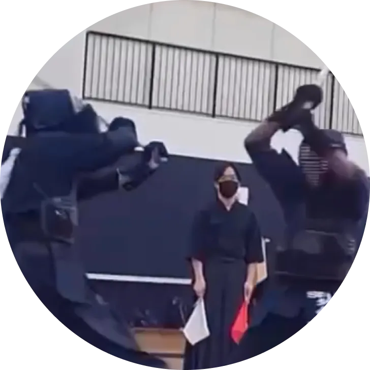 A kendo match in progress: two competitors and a shinpan (referee) holding red and white judging flags.